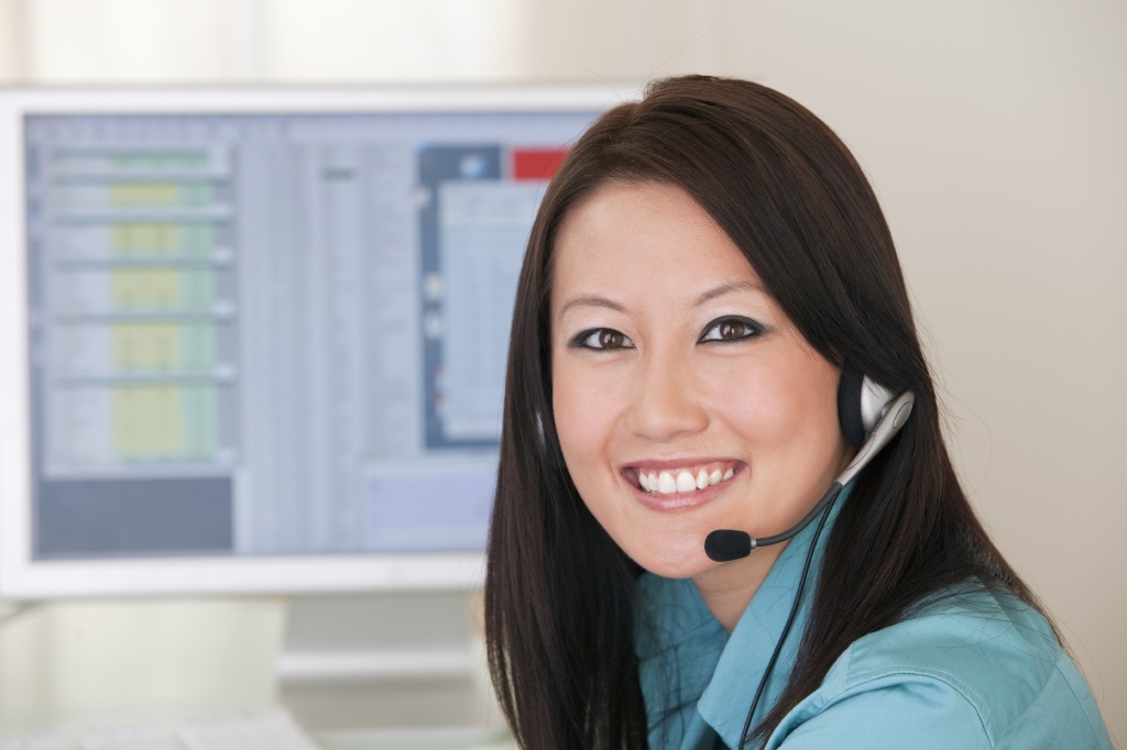 Smiling Asian woman with headset and computer monitor